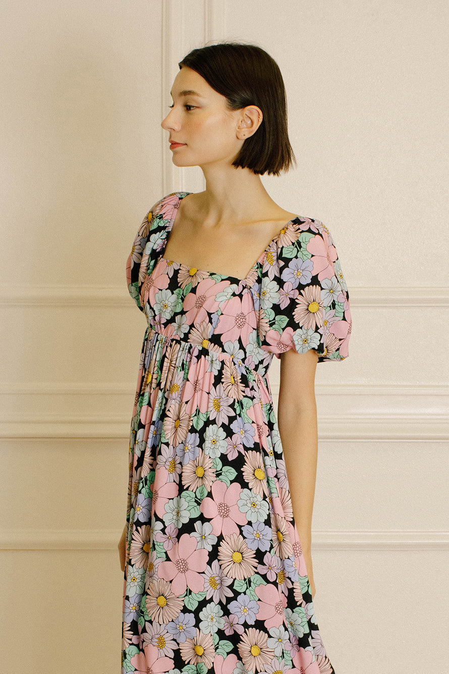 Side view of a woman wearing a pastel floral midi dress against a beige wall