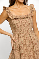 Woman wearing a beige floral dress with ruffled straps on a white background