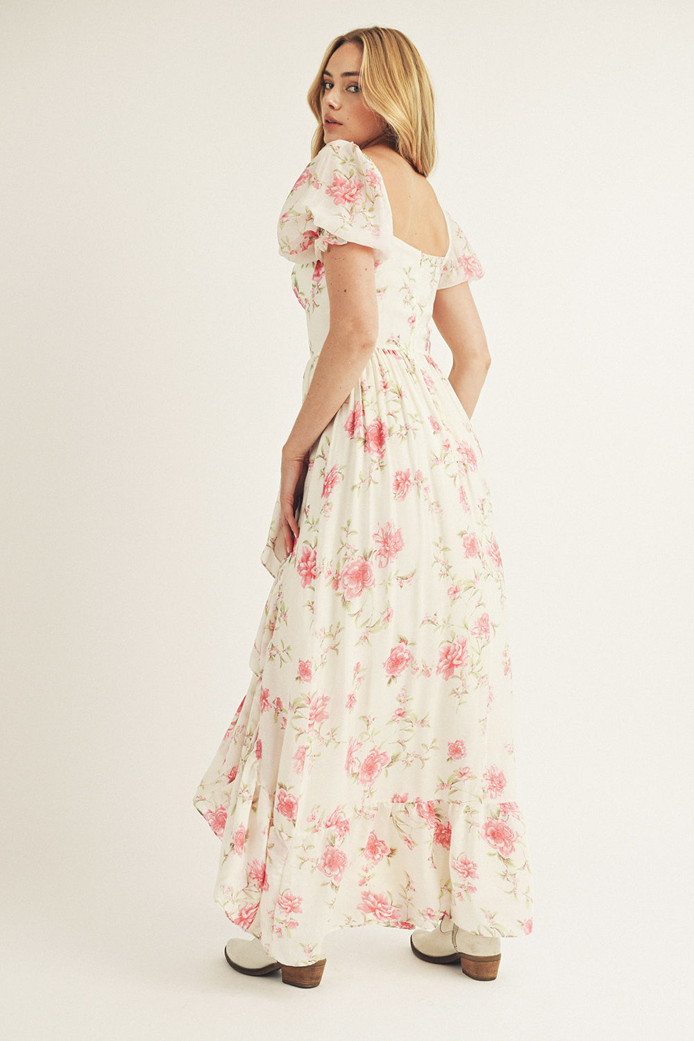 Back view of a woman wearing a floral dress and white cowboy boots on a plain background