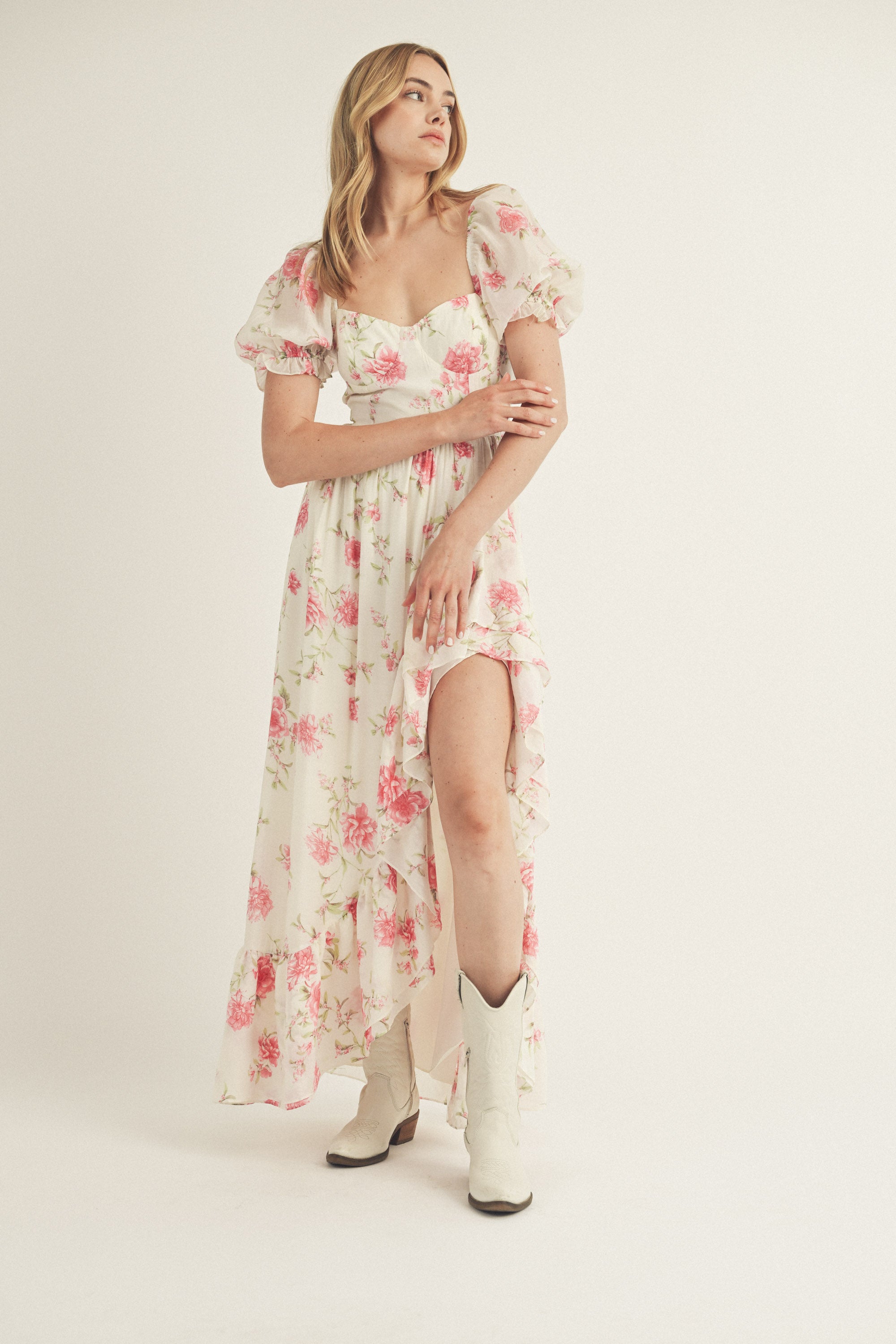 Woman wearing a floral dress and white cowboy boots on a plain background
