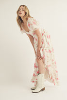Side view of a woman wearing a floral dress and white cowboy boots on a plain background