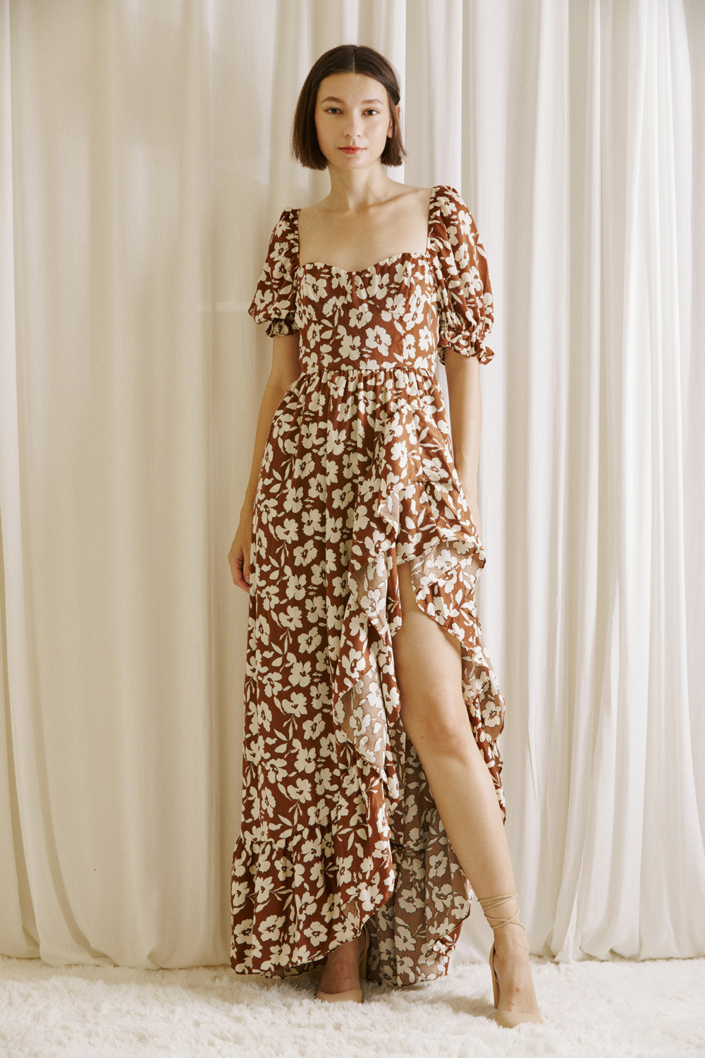 Woman wearing a brown and white floral dress standing against a white curtain backdrop
