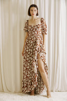 Woman wearing a brown and white floral dress standing against a white curtain backdrop