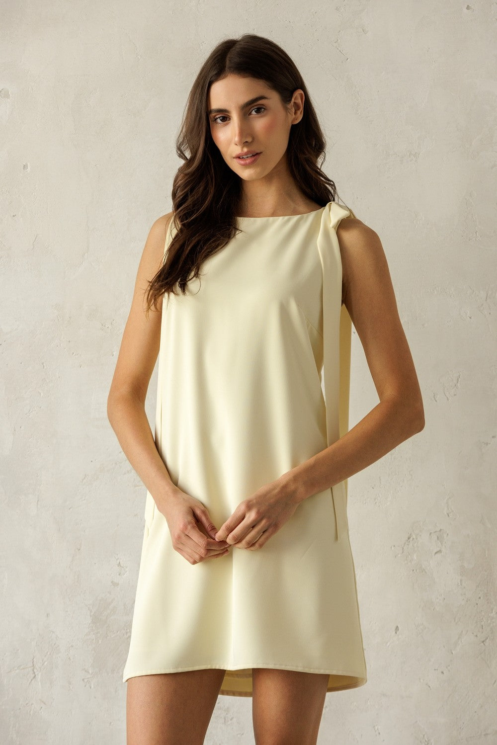Woman wearing a light yellow dress against a plain background