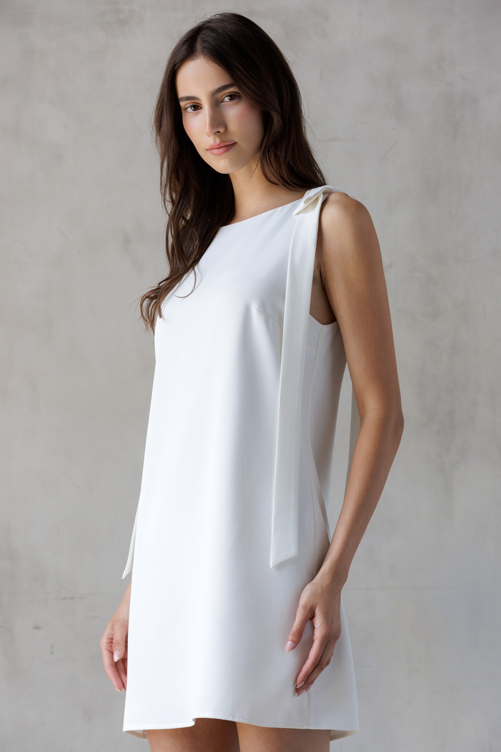 Woman wearing a white dress with a bow detail against a gray background
