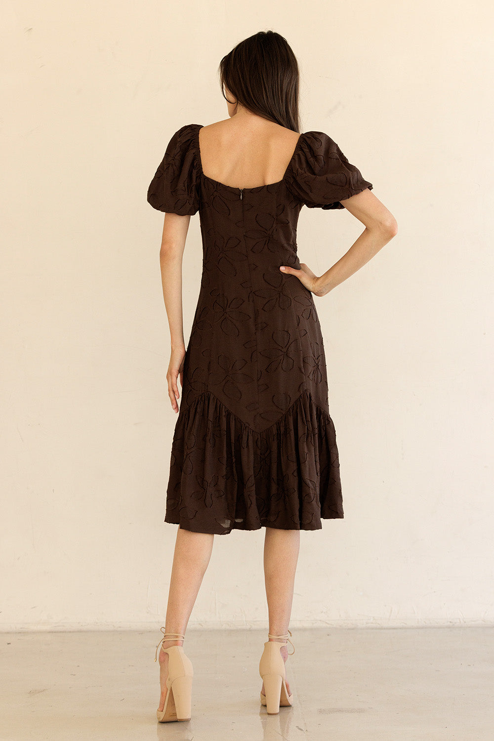 Woman wearing a brown dress with puff sleeves against a beige background
