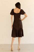 Woman wearing a brown dress with puff sleeves against a beige background