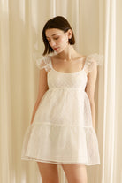 Woman wearing a white dress against a beige curtain background