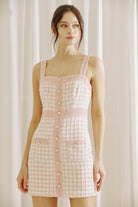 Woman wearing a pink checkered tweed dress against a white curtain background
