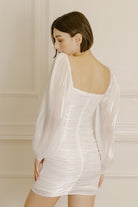 Side view of a woman wearing a white dress against a neutral background