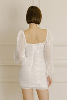 Back view of a woman wearing a white dress against a neutral background