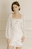 Woman wearing a white dress with diagonal bows on the upper front against a neutral background