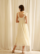 Back view of a woman wearing a cream midi dress standing in front of white curtains