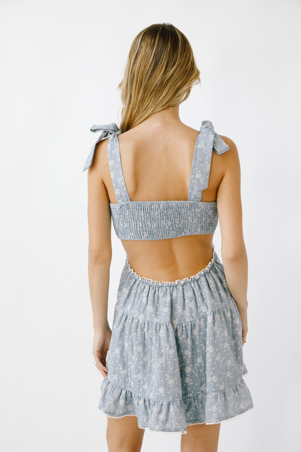 Back view of a woman wearing a blue denim floral dress against a white background