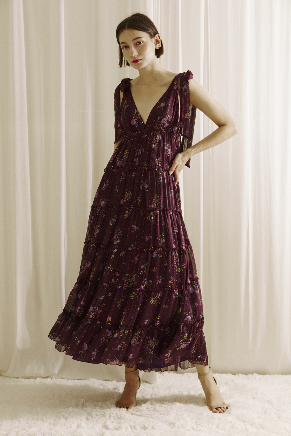 Woman wearing a plum base with an allover pink floral print maxi dress and beige heels on a white background