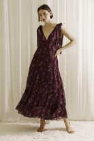 Woman wearing a plum base with an allover pink floral print maxi dress and beige heels on a white background