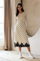 A model wearing a midi skirt that features a classic ivory and black polka dot print, A-line silhouette and romantic black lace-trimmed hem.