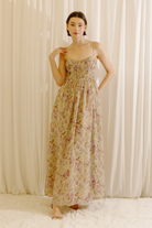 A model wearing a maxi dress with a romantic floral print, pleated bustier bodice, sweetheart neckline, adjustable straps, and a flowy maxi silhouette.