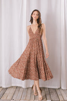 Woman wearing a floral dress standing against a white curtain.
