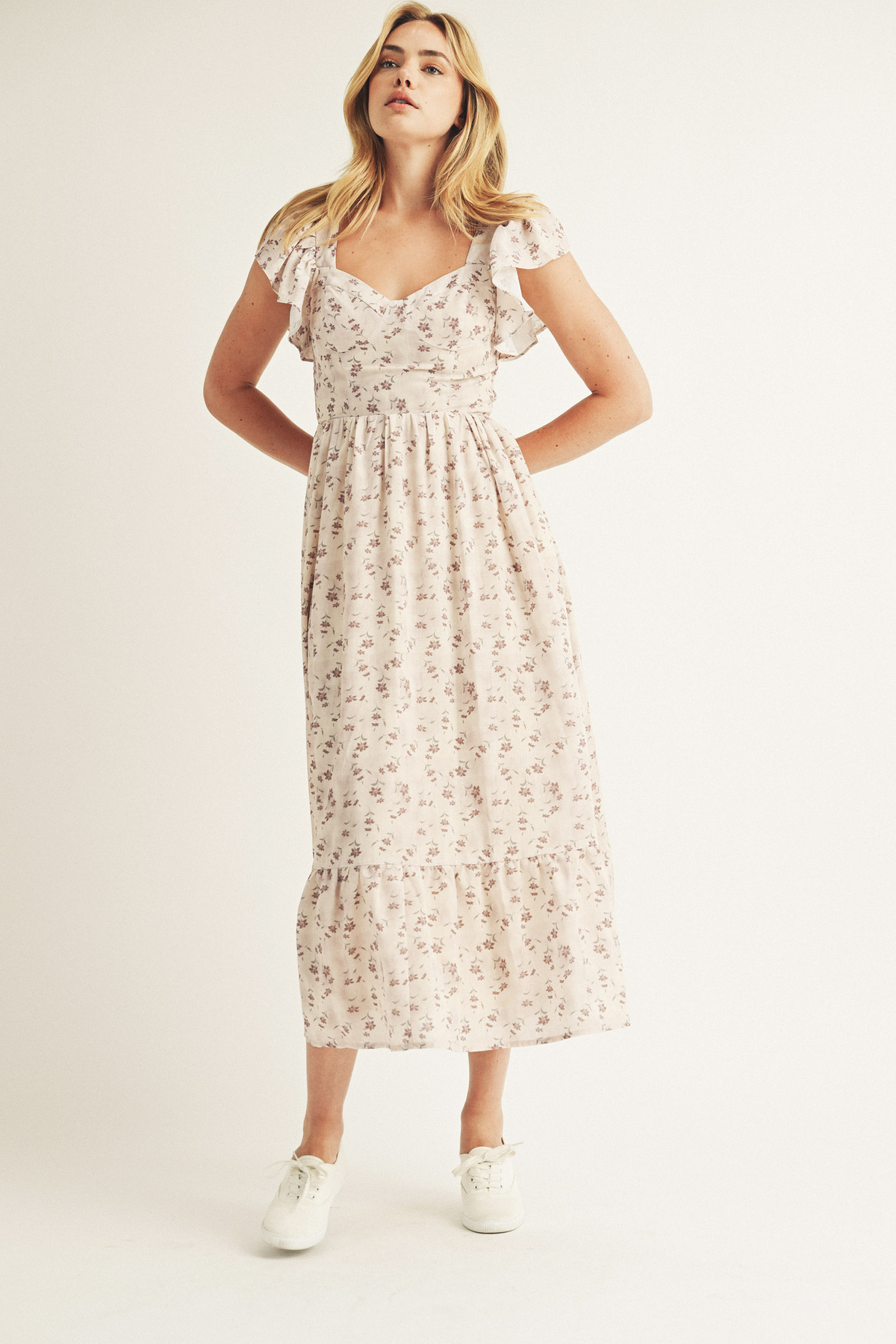 A woman modeling a floral print midi dress with a fitted bustier bodice, flutter sleeves, and a flowy midi skirt with a romantic ruffled hem.