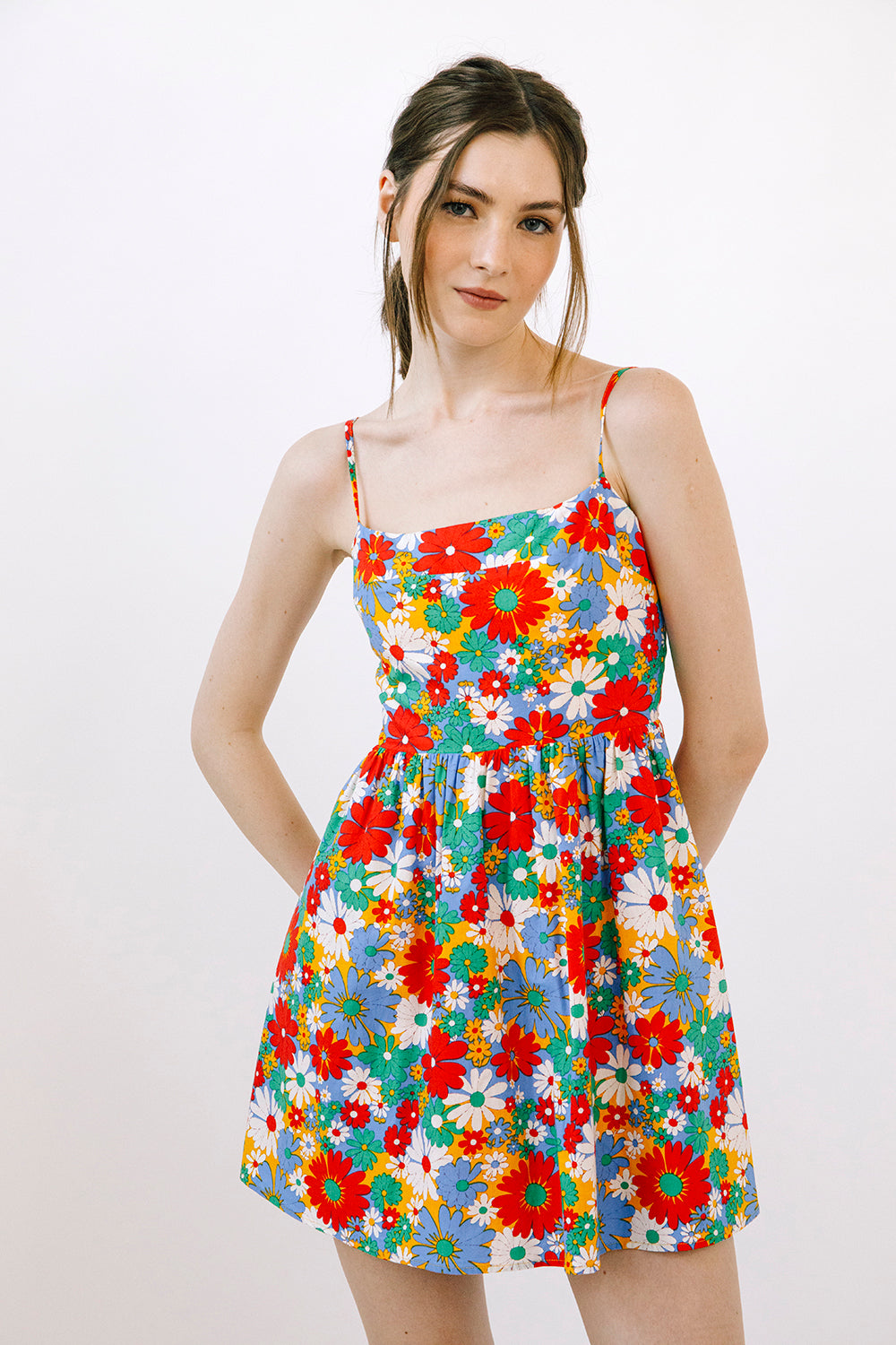 A woman modeling a sleeveless spaghetti-strap mini dress with a vibrant multicolor floral print on a white background, photographed against a clean white studio backdrop.