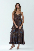 A model wearing a romantic brown maxi dress with blue floral print, V-neckline, empire waist, and cascading ruffle tiers for an effortless flowy look.