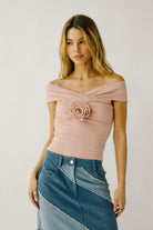 Woman wearing a pink off-shoulder top with a floral detail and a blue patchwork skirt on a plain background