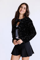 Woman wearing a black sequin jacket with two bows and black skirt on a white background