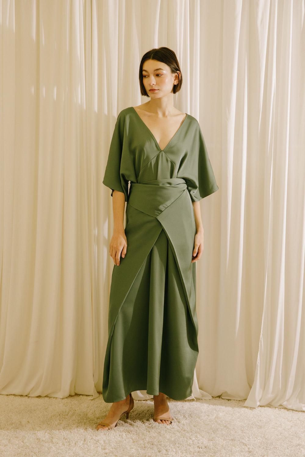 Woman wearing a green dress standing against a beige curtain backdrop