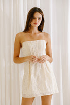 A woman wearing a strapless, floral embroidered corset mini dress in a cream color.