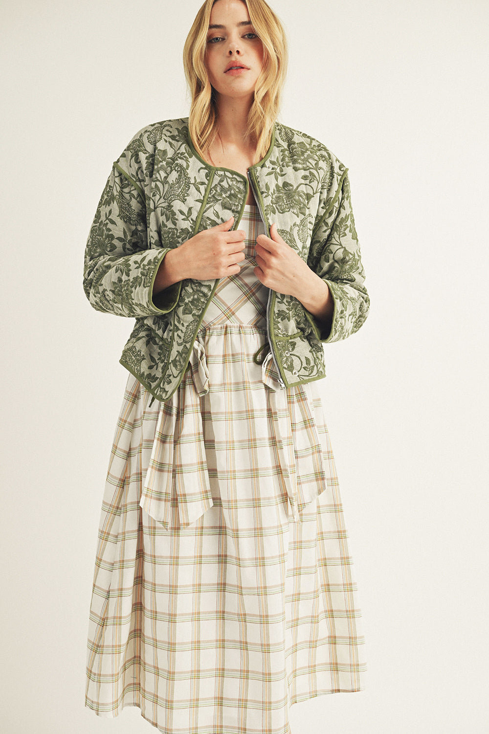 Woman wearing a green patterned jacket over a plaid dress on a white background
