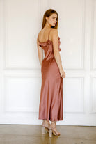 Back view of a woman wearing a mauve satin dress against a white paneled wall.