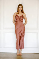 Woman wearing a mauve satin dress against a white paneled wall.