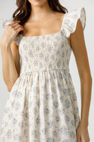 Woman wearing a cream and blue floral dress with ruffled sleeves on a plain background