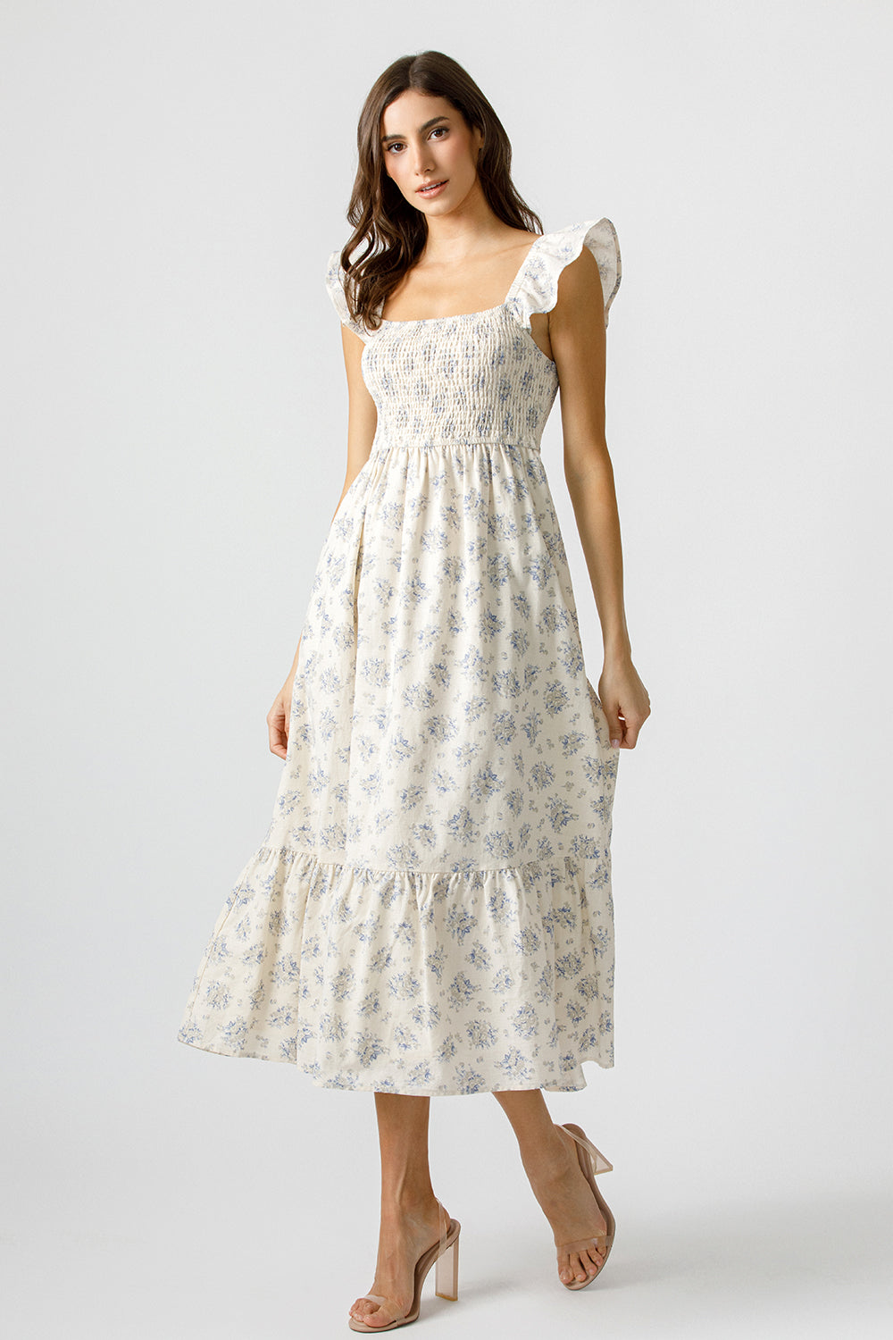 Woman wearing a cream and blue floral dress on a plain background