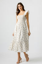 Woman wearing a cream and blue floral dress on a plain background