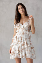 Woman wearing a beige and brown floral dress against a plain background