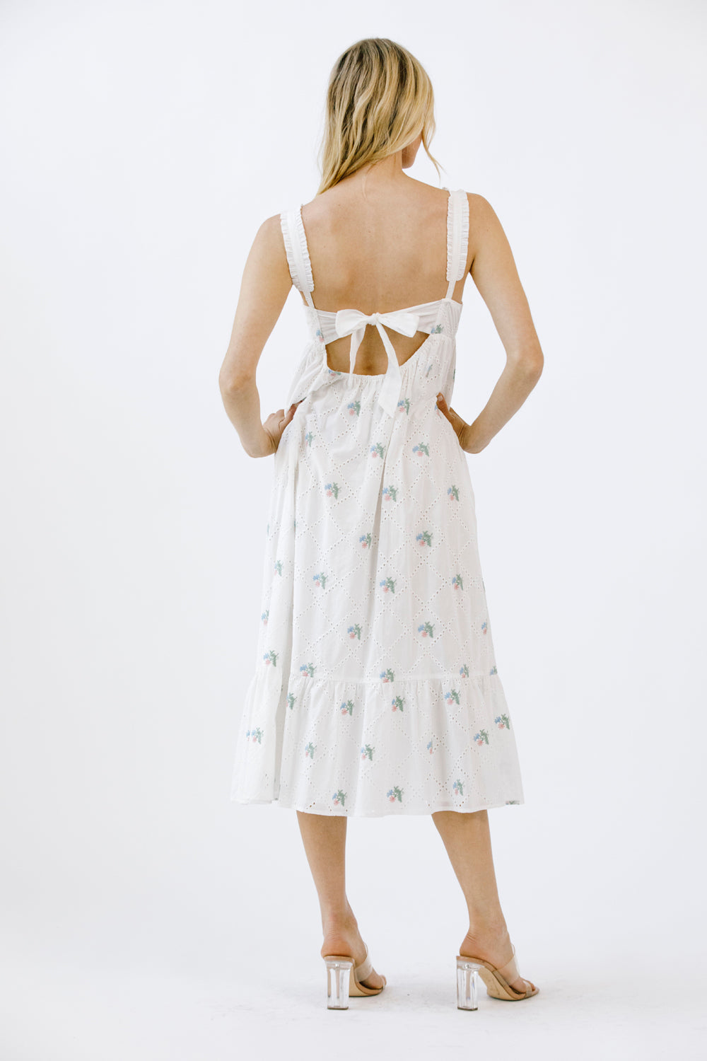 Back view of a woman wearing a white dress with a subtle pattern on a white background
