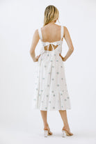 Back view of a woman wearing a white dress with a subtle pattern on a white background