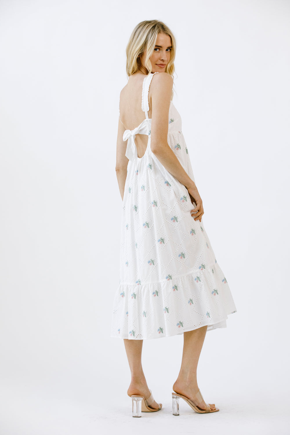 Side view of a woman wearing a white dress with a subtle pattern on a white background