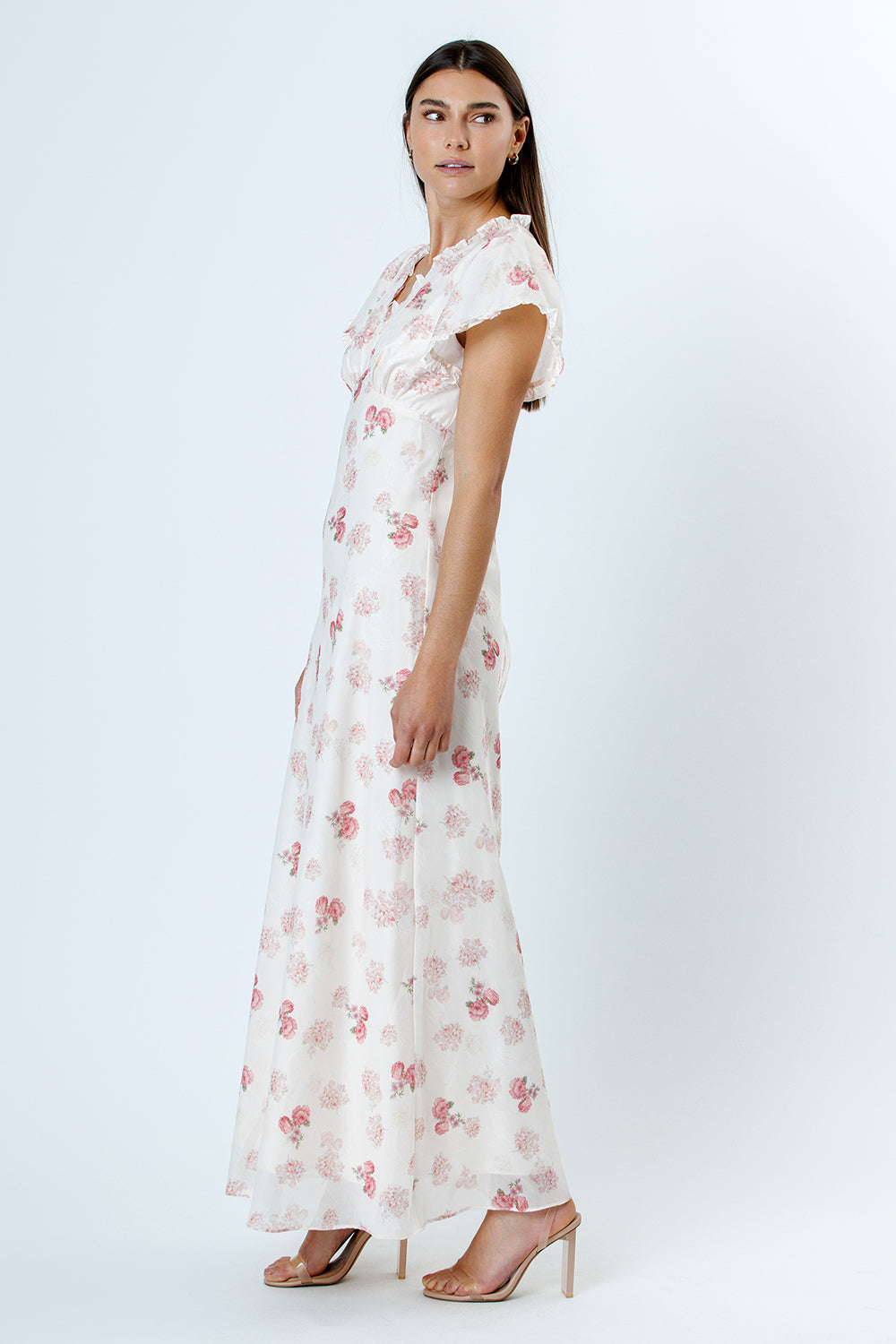 Side view of a woman wearing a pink and white floral dress with flutter sleeves on a white background