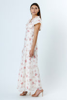 Side view of a woman wearing a pink and white floral dress with flutter sleeves on a white background