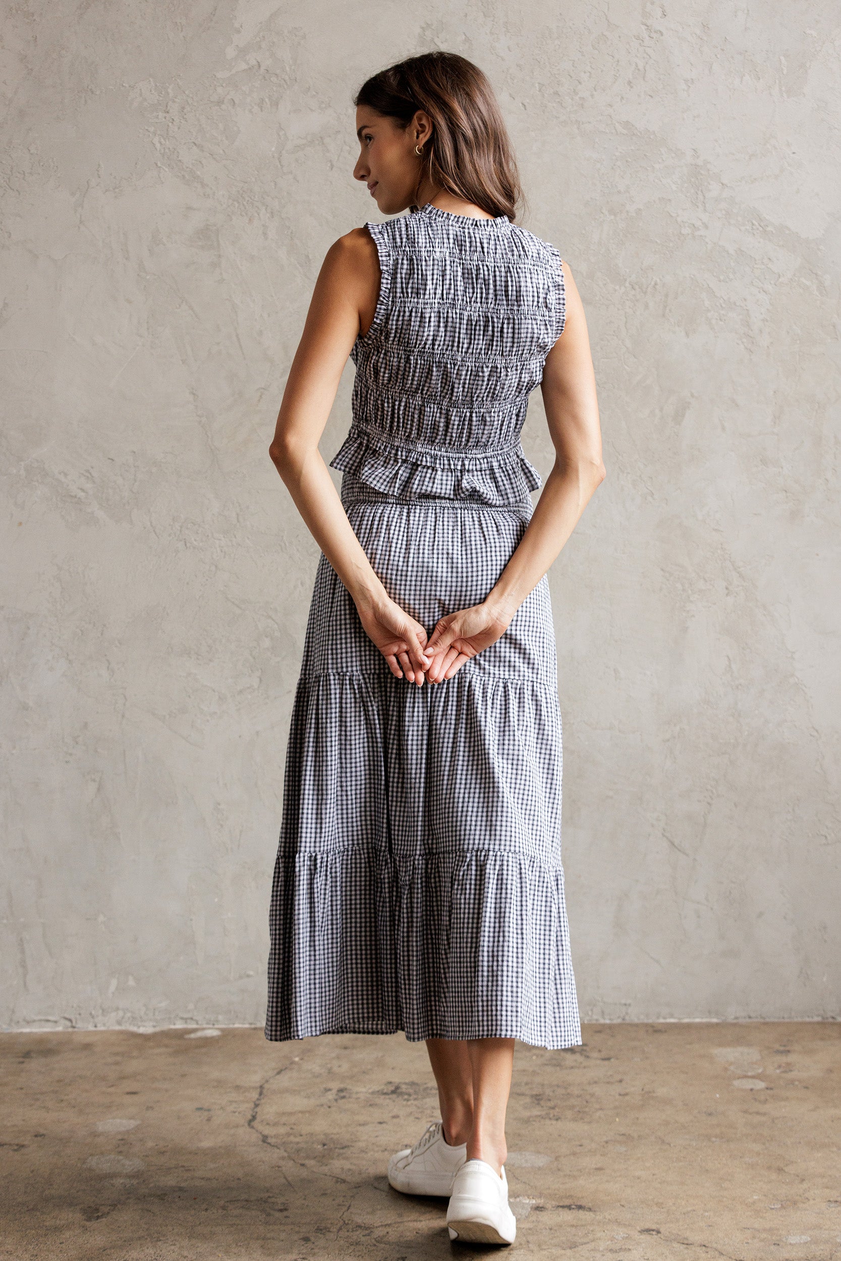 Back view of a woman wearing a checkered set of a top and a skirt standing against a plain wall.