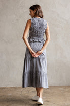 Back view of a woman wearing a checkered set of a top and a skirt standing against a plain wall.