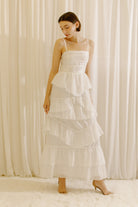 Woman wearing a white tiered maxi dress against a plain background