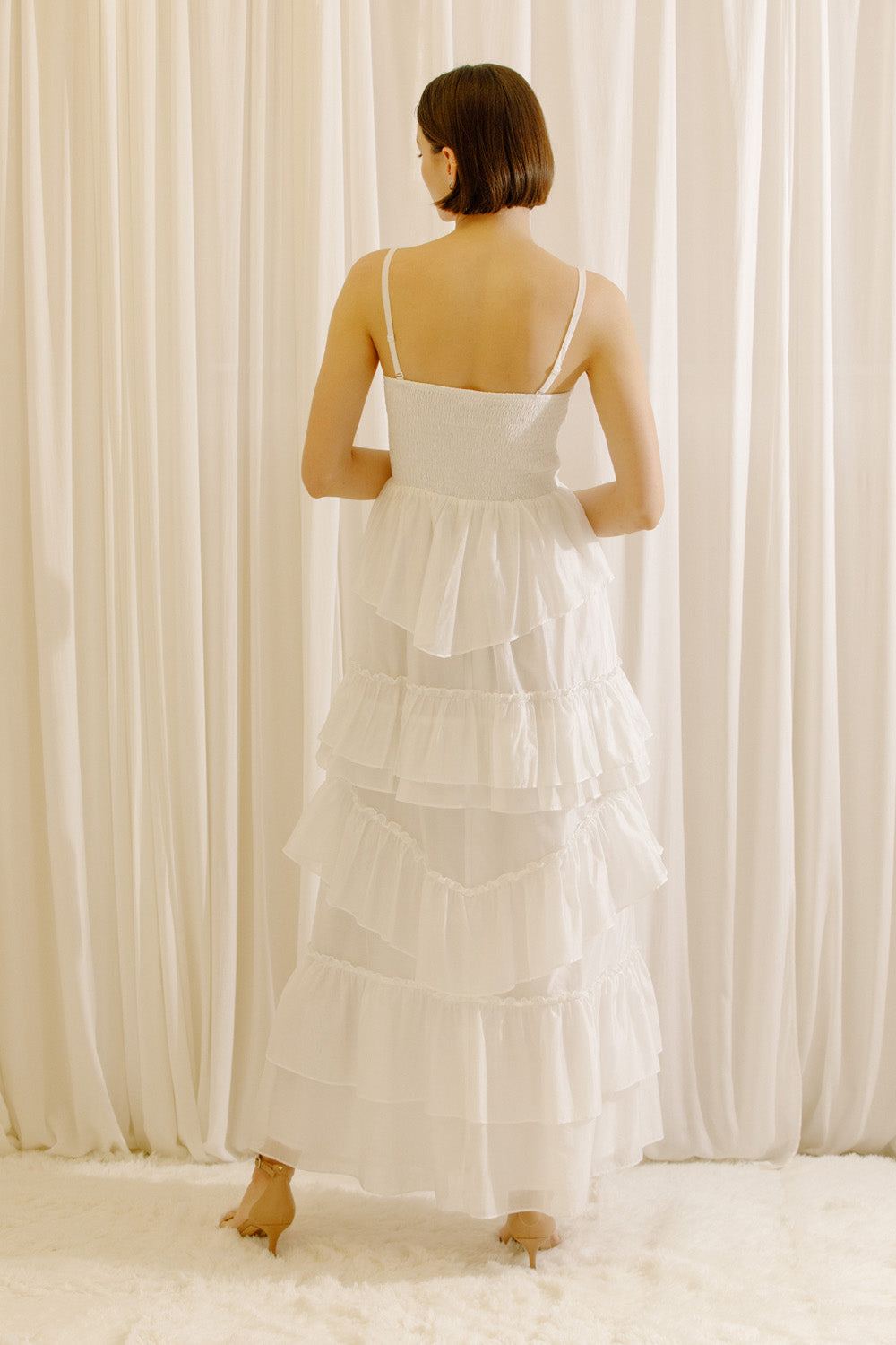 Back view of a woman wearing a white maxi dress standing in front of sheer curtains