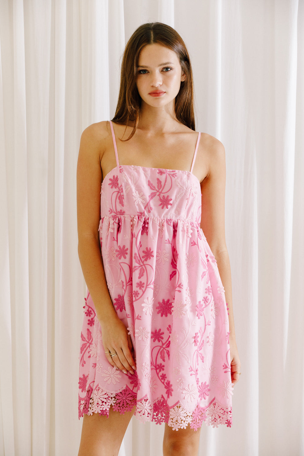 Woman wearing a pink floral dress against a white curtain background