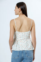 A woman viewed from behind wearing a floral peplum top and blue jeans on a white background