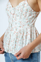 A close-up of a woman wearing a sleeveless white camisole top with a delicate pink and green floral print, paired with blue jeans.