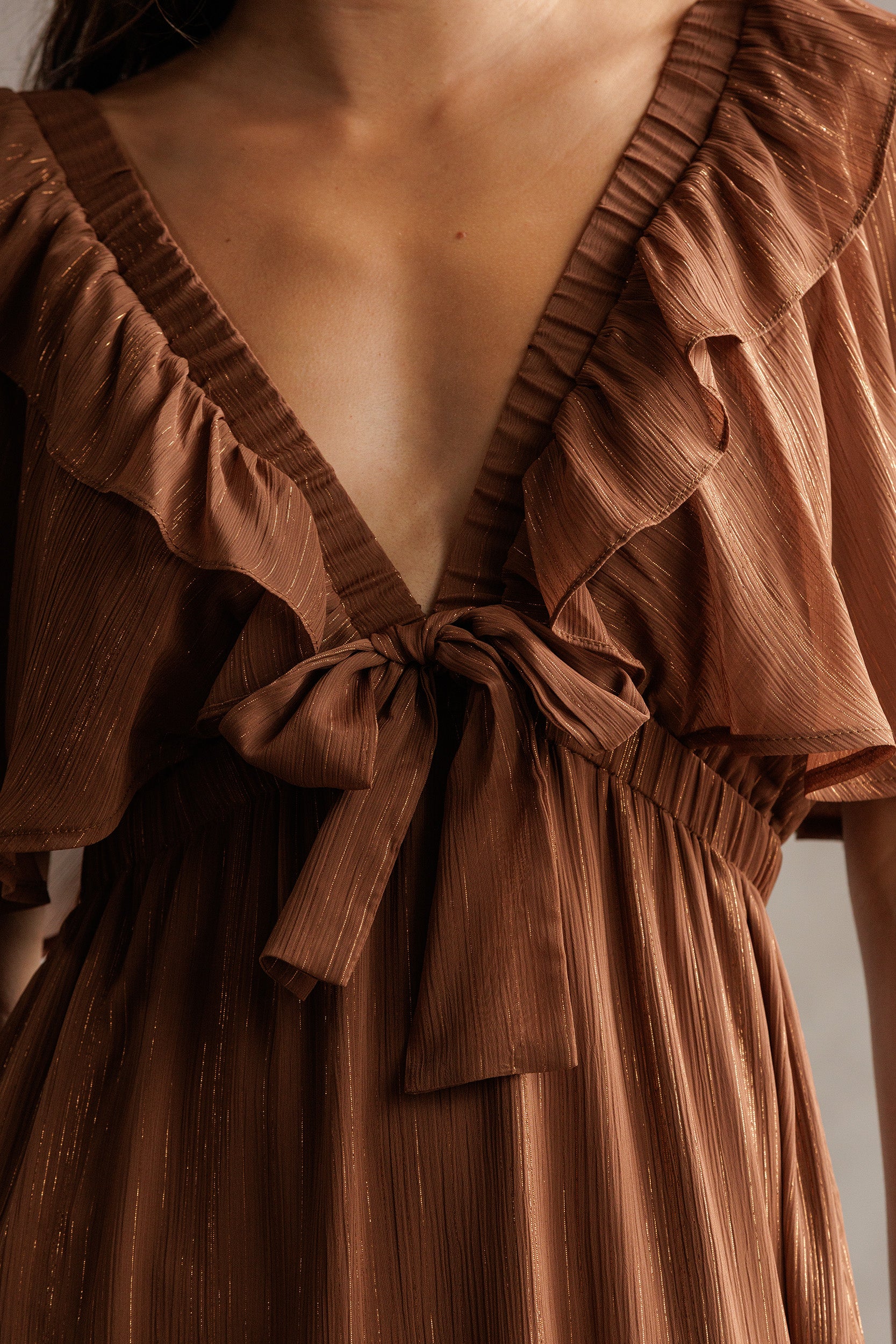 Brown dress with ruffled details and a tie waist on a neutral background